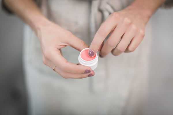 Closeup of a finger scrubbing a pink lip balm pot